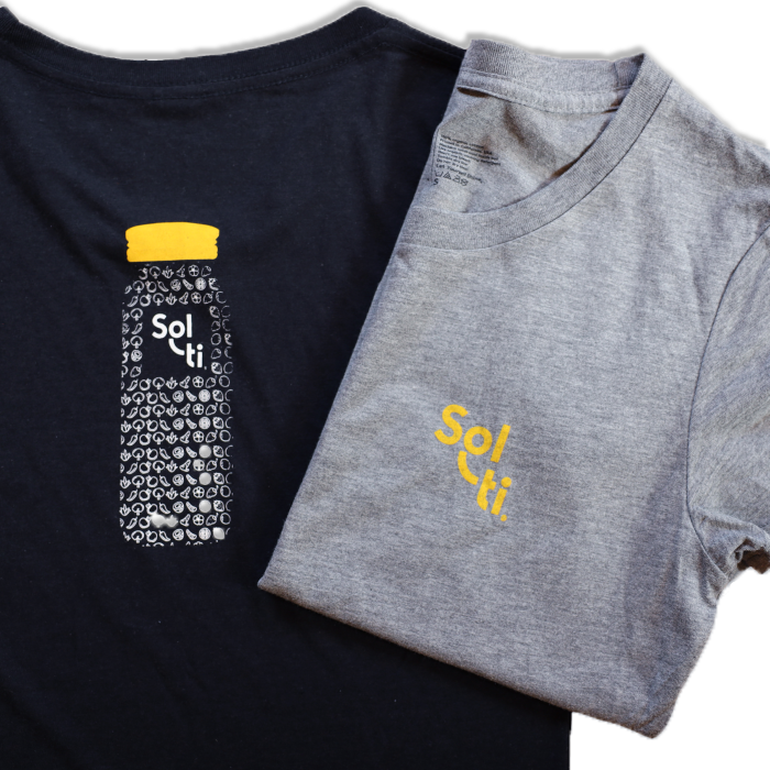 Two Youth Organic Cotton Tees, one in black and one in gray, each featuring the Sol-ti logo with orange text; the black tee also has a design of a bottle filled with SuperFoods and a orange cap on the back.