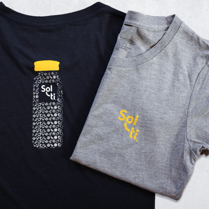 Two Youth Organic Cotton Tees, one in black and one in gray, each featuring the Sol-ti logo with orange text; the black tee also has a design of a bottle filled with SuperFoods and a orange cap on the back.