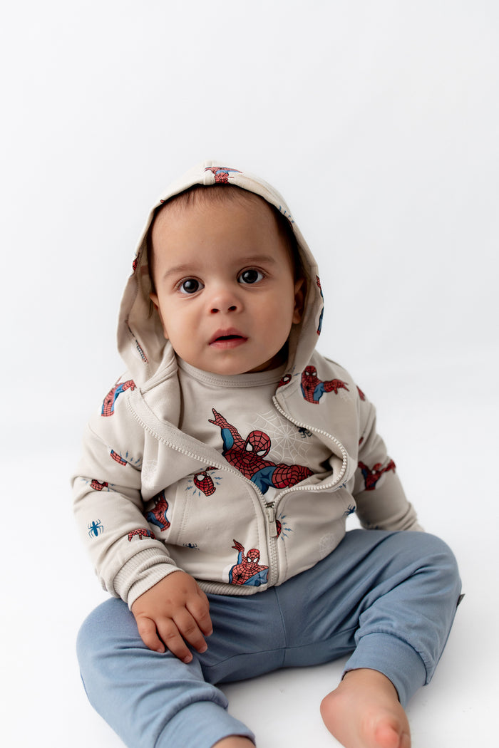 toddler sitting down wearing a spiderman jacket with the hoodie on his head.