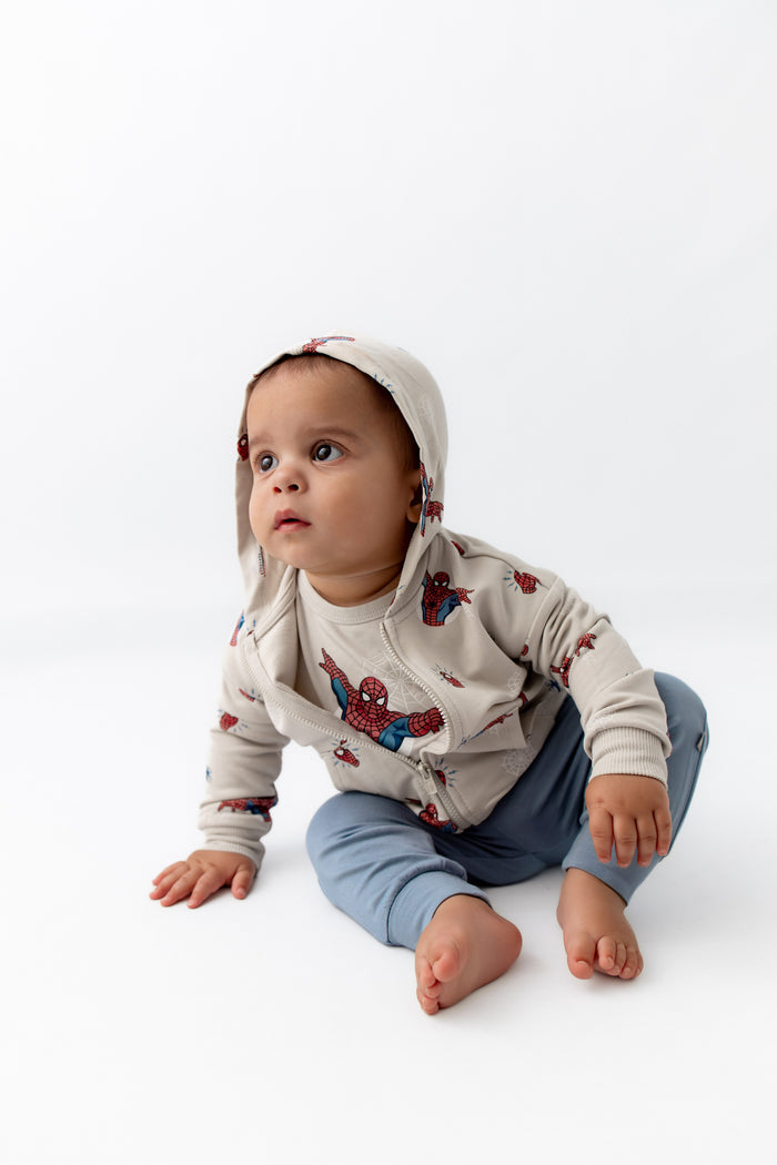Toddler sitting down leaning over wearing a spiderman jacket with the hoodie on is head.