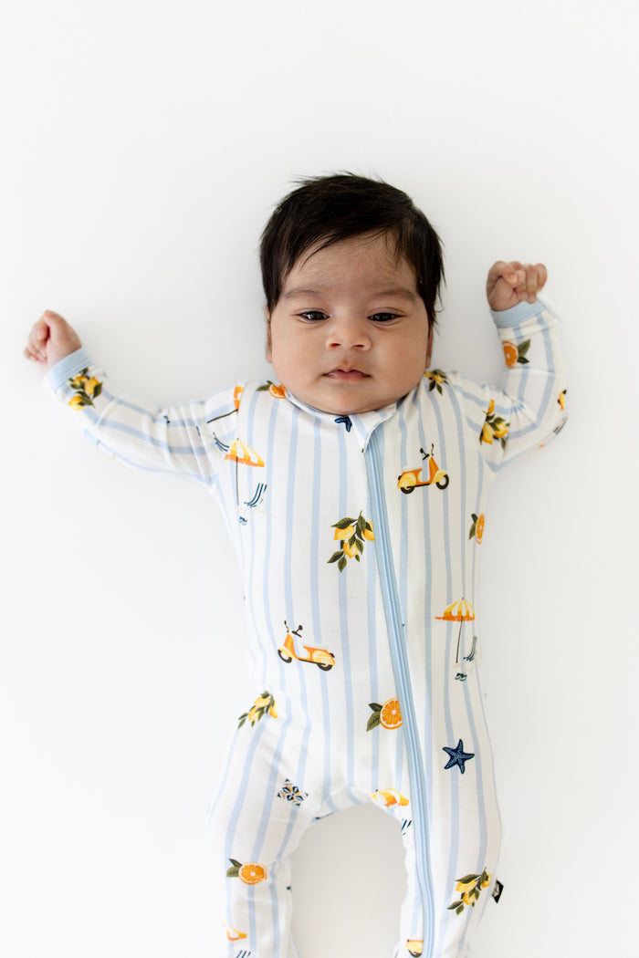 Close up of newborn wearing the Zippered Footie in Amalfi Coast laying on a white surface