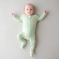 Baby wearing a light green zippered footie on a plain background