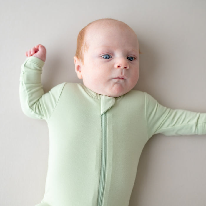 Baby wearing a light green zippered footie  on a plain background