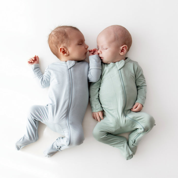 Two newborns sleeping in Zippered Footies in Fog and Sage
