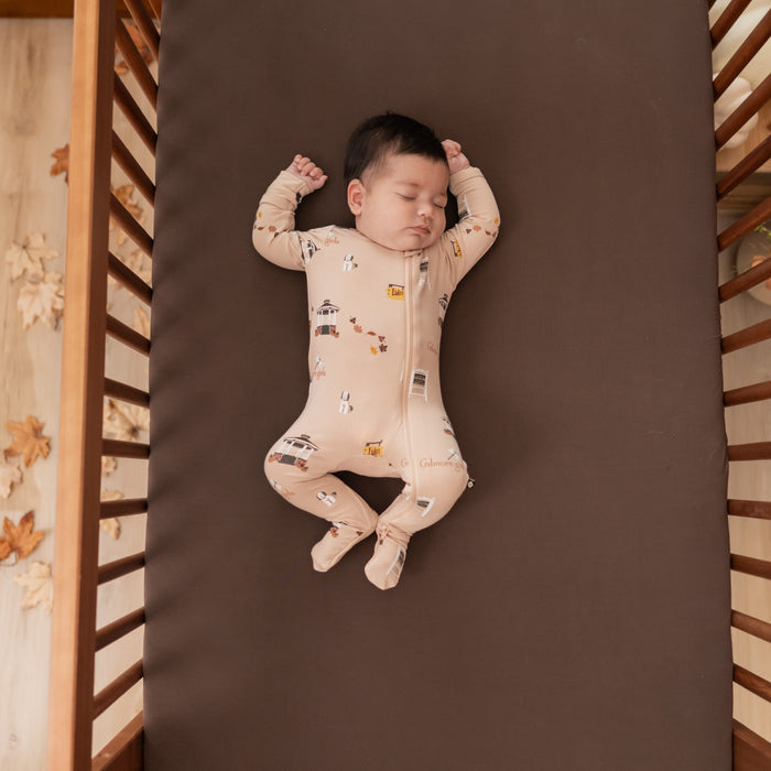 Sleeping infant laying in a crip on an Espresso crib sheet wearing the Zippered Footie in Gilmore Girls