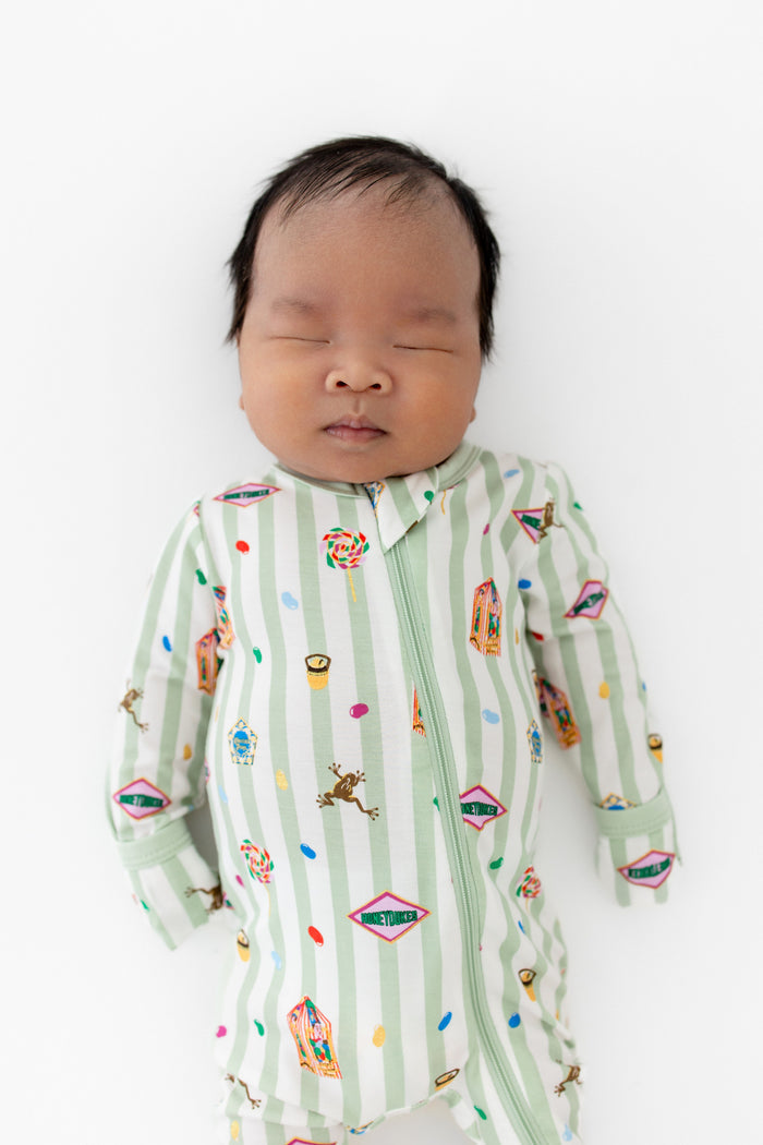 Baby sleeping in a green and white striped zippered footie with colorful Harry Potter patterns on a white background
