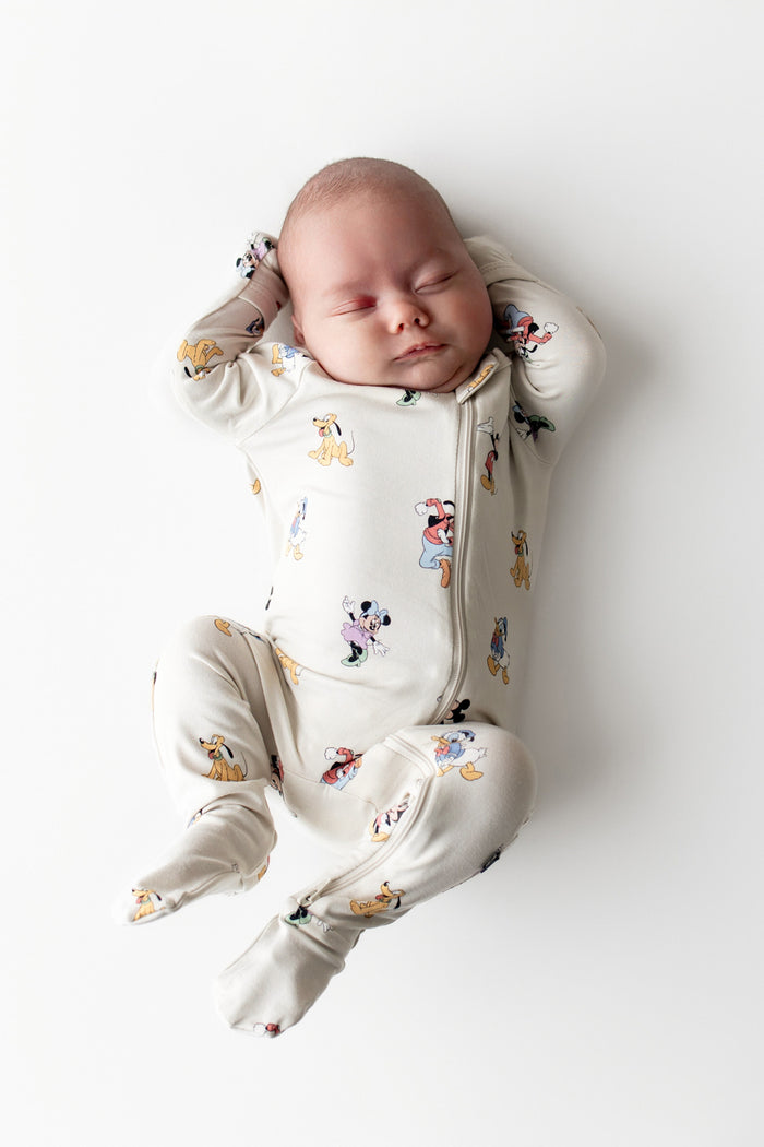 Baby sleeping in a cream footed onesie with mickey cartoon character print on a white background