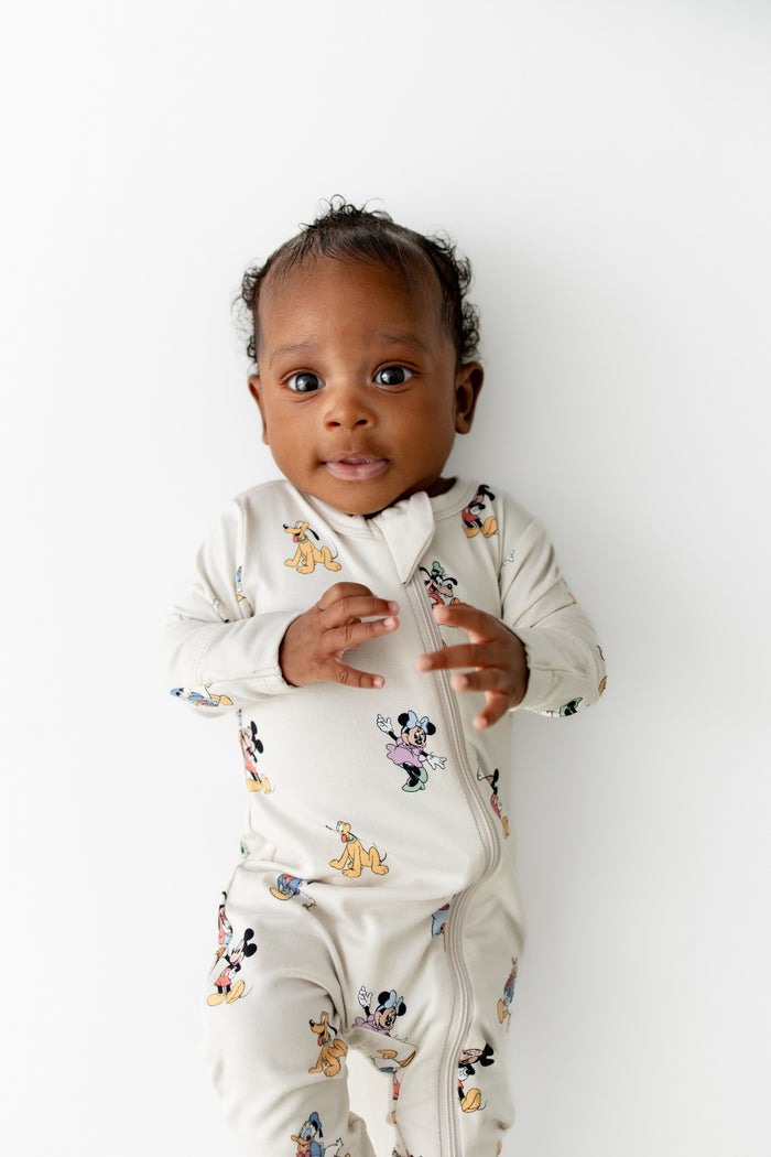 Baby wearing a cream footie with cartoon character prints on a white background