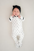 Baby sleeping in midnight polka dot print zippered footie with black bow headband on a beige background