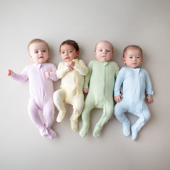 Four infants laying size by side wearing the zippered footies in spring colors