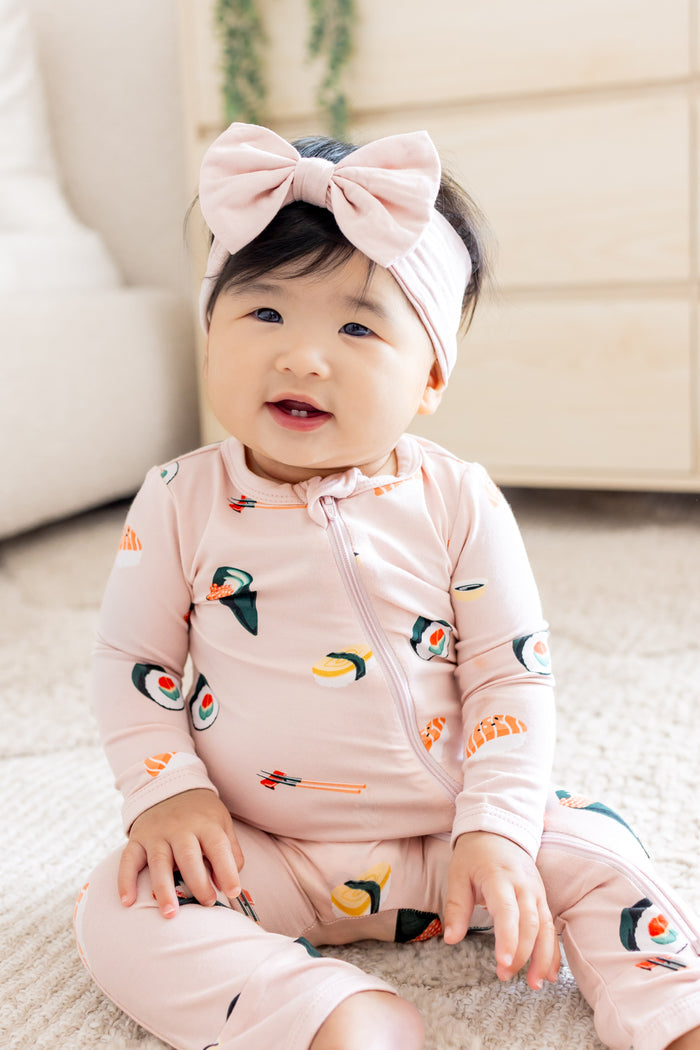 Baby sitting up in blush sushi zipper romper and pink bow